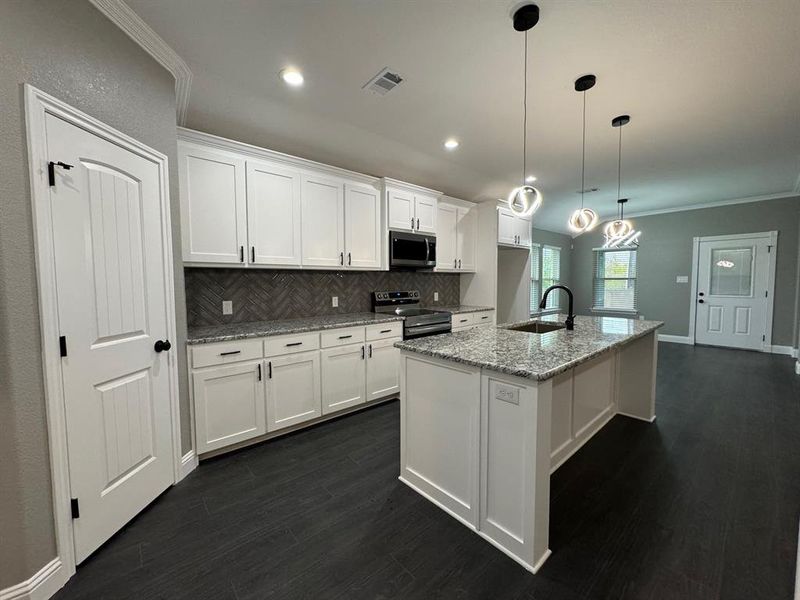 Kitchen featuring sink, stainless steel appliances, light stone counters, a kitchen island with sink, and white cabinets