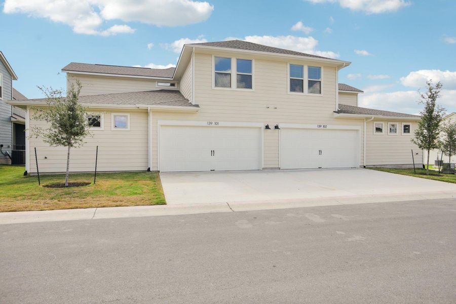 View of front of property with an attached garage, concrete driveway, roof with shingles, and a front yard