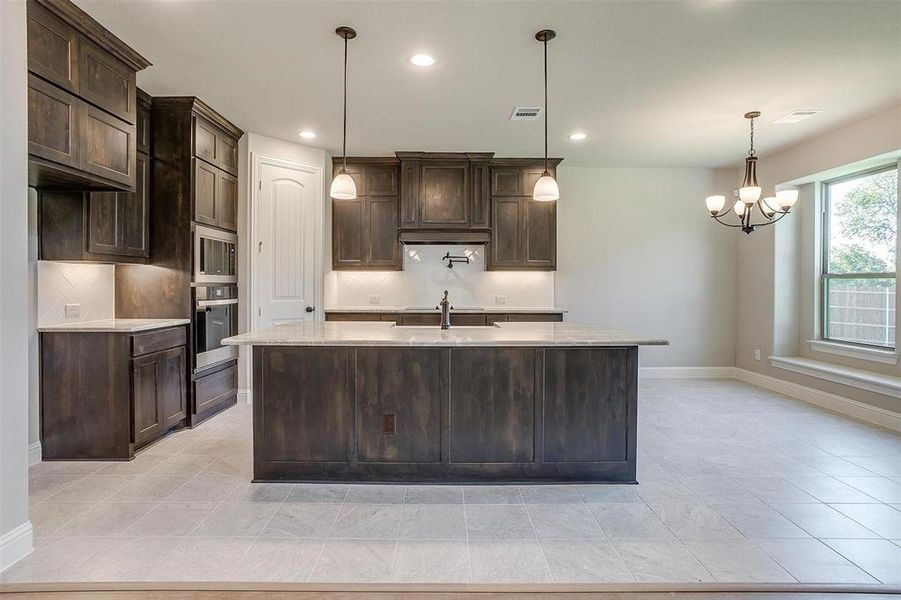 Kitchen with backsplash, stainless steel appliances, dark brown cabinetry, and a center island with sink