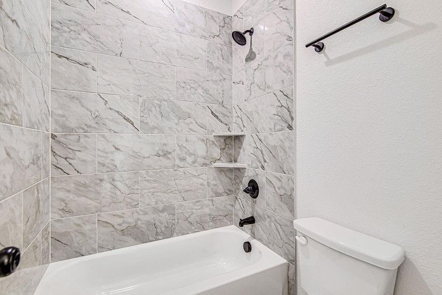 Bathroom with shower / bath combination, toilet, and a textured wall