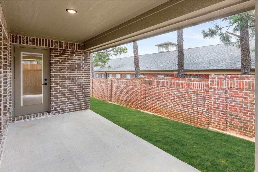 Covered back patio with concrete floor, brick walls, small grass yard, and door entry to home