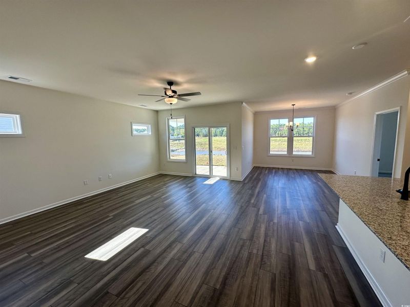 Unfurnished living room featuring plenty of natural light, dark wood finished floors, a chandelier, ceiling fan, and crown molding Unfurnished living room featuring plenty of natural light, dark wood finished floors, a chandelier, ceiling fan, and crown molding