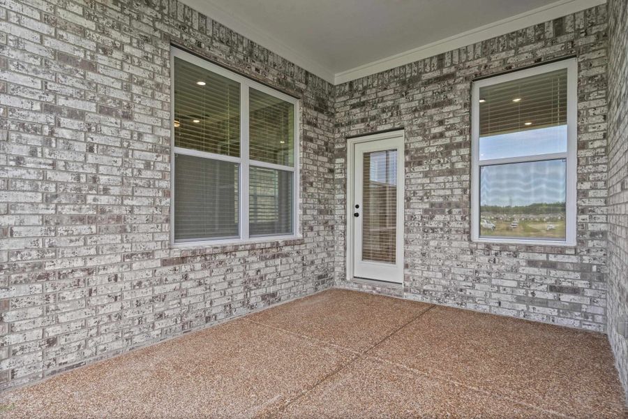 Covered patio featuring a light-colored brick exterior, a textured concrete floor, and white trim Covered patio featuring a light-colored brick exterior, a textured concrete floor, and white trim