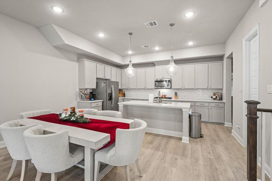 Kitchen with a center island with sink, stainless steel appliances, light hardwood / wood-style flooring, decorative light fixtures, and white cabinets