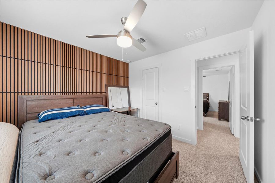 A secondary bedroom features a striking wood-accent wall with vertical detailing, complemented by a clean layout and a ceiling fan for added comfort. A secondary bedroom features a striking wood-accent wall with vertical detailing, complemented by a clean layout and a ceiling fan for added comfort.