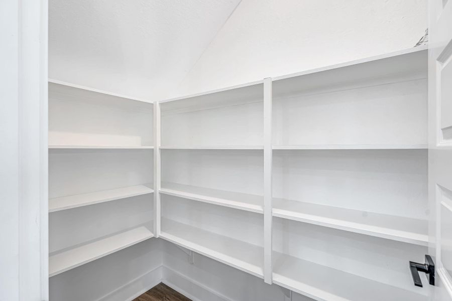 Spacious walk-in pantry conveniently located across from the kitchen, featuring multiple built-in shelves for organized storage.