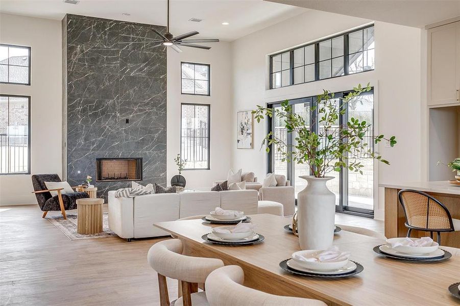 Dining space with a healthy amount of sunlight, light wood-type flooring, a high ceiling, and a premium fireplace