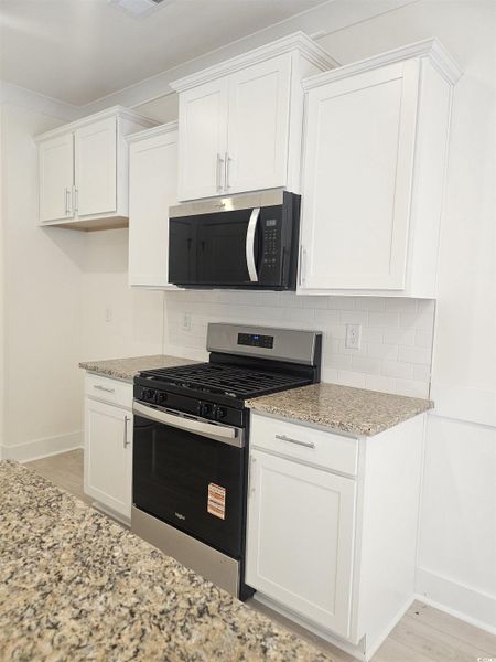 Kitchen with appliances with stainless steel finishes, white cabinetry, backsplash, and light stone counters Kitchen with appliances with stainless steel finishes, white cabinetry, backsplash, and light stone counters