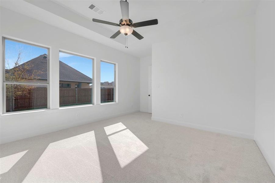 Spacious room featuring three large windows, light-colored carpet flooring, a ceiling fan with integrated lighting, and crisp white walls Spacious room featuring three large windows, light-colored carpet flooring, a ceiling fan with integrated lighting, and crisp white walls