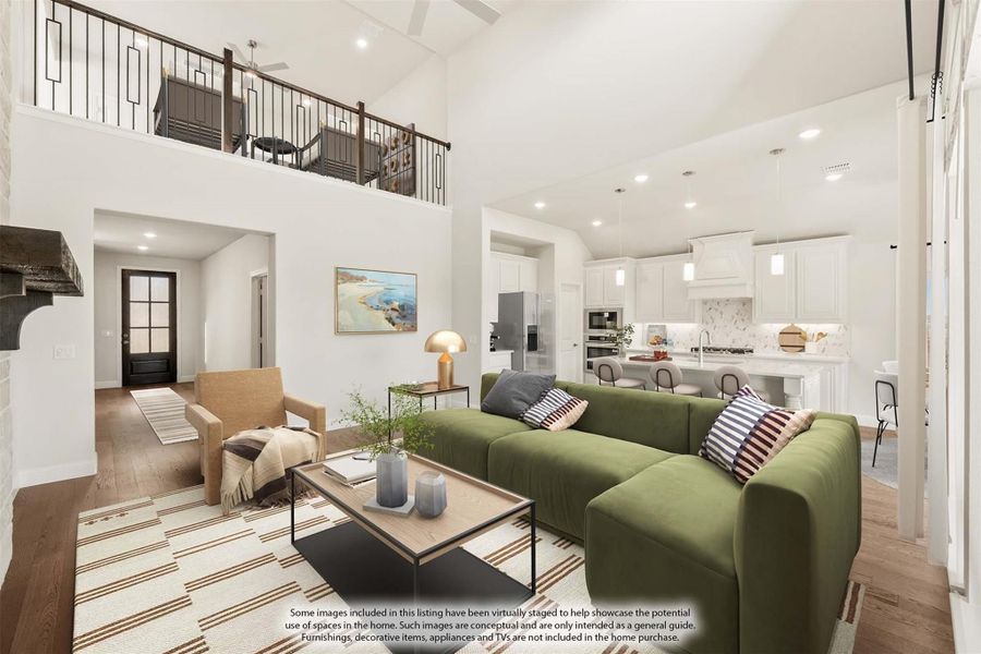 Open-concept living room with two-story ceiling, green sectional sofa, and white kitchen visible in background
