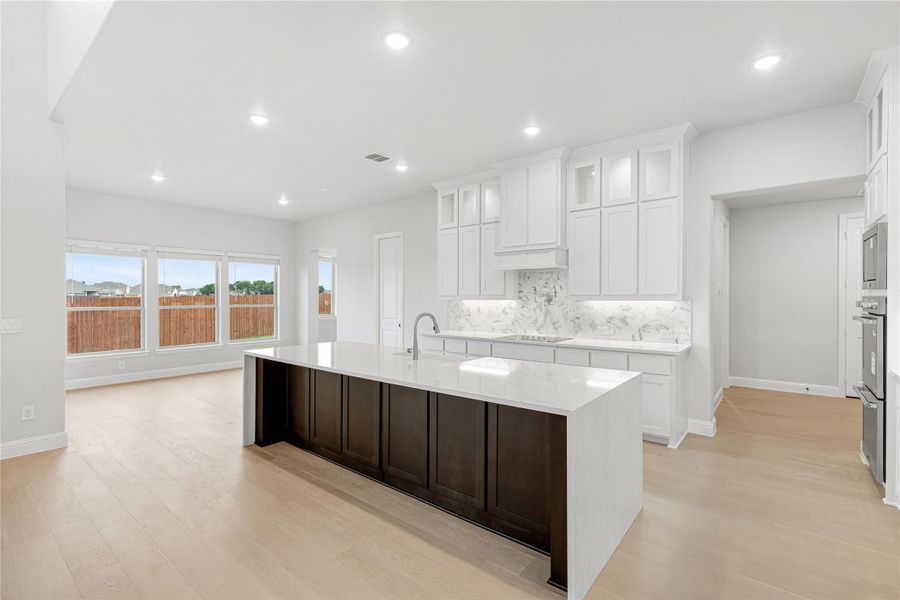 Open kitchen with large dark wood island, white quartz countertops, white cabinets, marble backsplash, and light hardwood floors