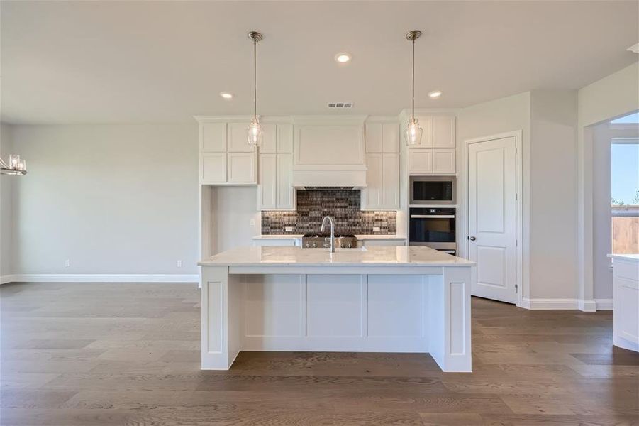 Kitchen featuring an island with sink, hanging light fixtures, hardwood / wood-style flooring, and stainless steel appliances