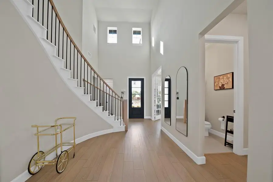 Spacious entryway featuring wood-finish flooring, a grand curved staircase with black iron balusters, a high ceiling, and multiple transom windows providing natural illumination Spacious entryway featuring wood-finish flooring, a grand curved staircase with black iron balusters, a high ceiling, and multiple transom windows providing natural illumination