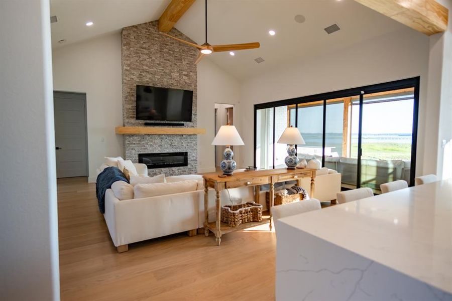 Living room featuring beam ceiling, a fireplace, light wood-style flooring, high vaulted ceiling, and recessed lighting Living room featuring beam ceiling, a fireplace, light wood-style flooring, high vaulted ceiling, and recessed lighting