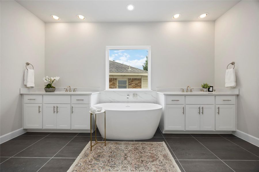 Step into an oasis featuring a vessel tub set between dual vanities, framed by custom wood cabinets and quartz countertops, for an unwavering indulgence.