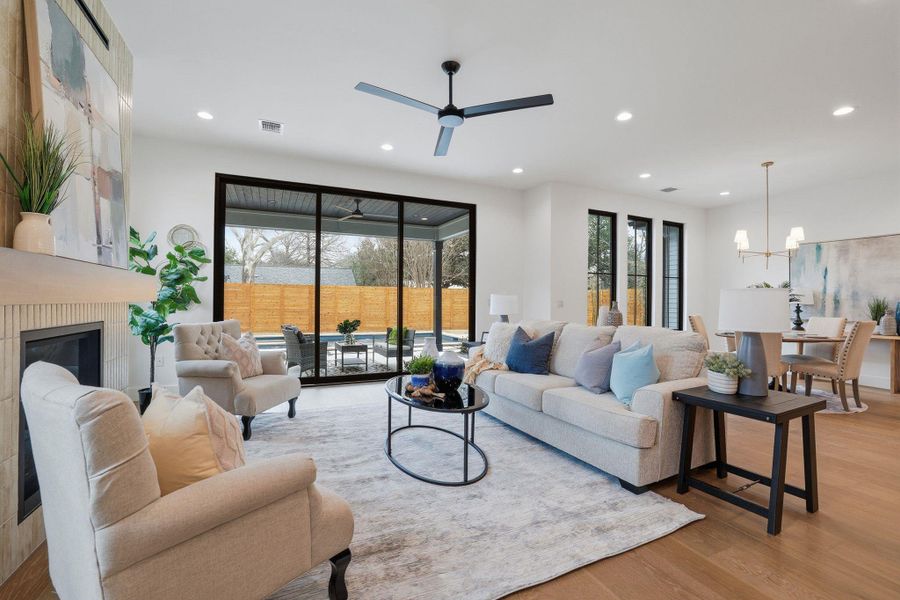 Living room featuring light wood-type flooring, a large fireplace, a ceiling fan, and hanging lights