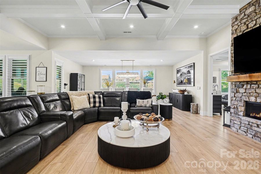 This open-concept living area features a dramatic floor-to-ceiling stone fireplace, elegant coffered ceilings with a large industrial fan.