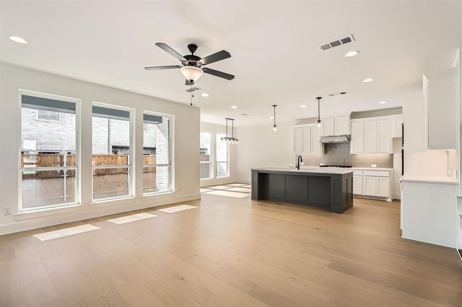 Kitchen with white cabinetry, an island with sink, light hardwood / wood-style flooring, pendant lighting, and decorative backsplash