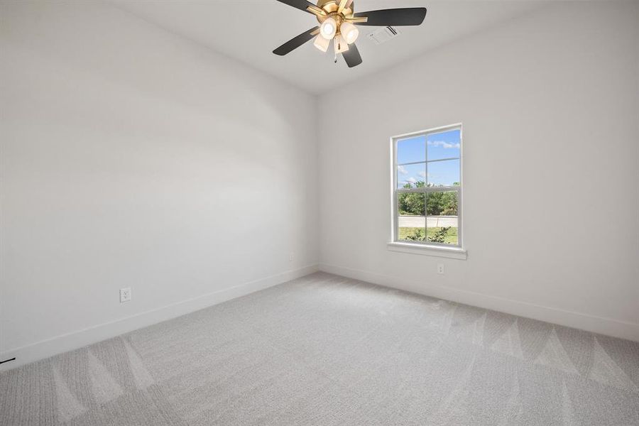 Bright interior room featuring a window with exterior views, light gray carpeting, and a ceiling fan with integrated lighting