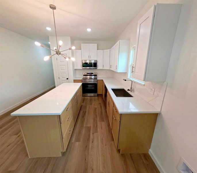 Kitchen featuring appliances with stainless steel finishes, light wood-type flooring, a chandelier, a center island, and white cabinetry Kitchen featuring appliances with stainless steel finishes, light wood-type flooring, a chandelier, a center island, and white cabinetry
