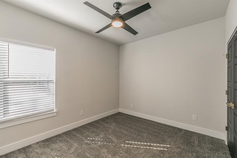 Empty room with a wealth of natural light, ceiling fan, and dark carpet