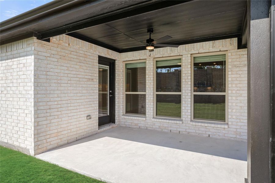 Covered back patio with ceiling fan, concrete floor, and brick exterior wall with large windows and door. Covered back patio with ceiling fan, concrete floor, and brick exterior wall with large windows and door.