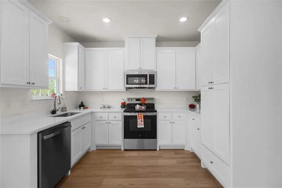 Kitchen with appliances with stainless steel finishes, light wood finished floors, white cabinetry, and recessed lighting