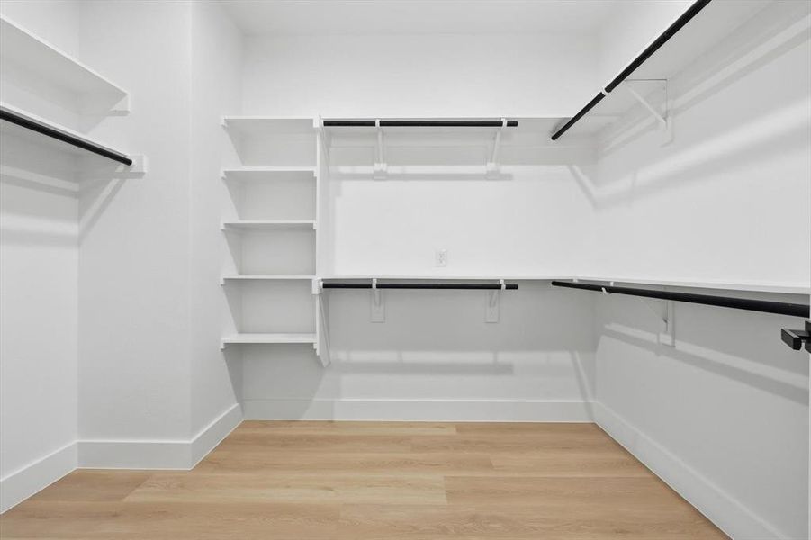 Walk-in closet featuring white walls, wood-finish flooring, multiple shelving units, and black clothing rods Walk-in closet featuring white walls, wood-finish flooring, multiple shelving units, and black clothing rods