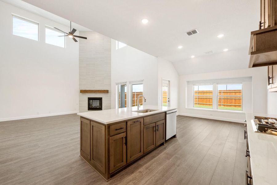 Open kitchen with wood island, white countertops, and vaulted ceiling open to living area with fireplace