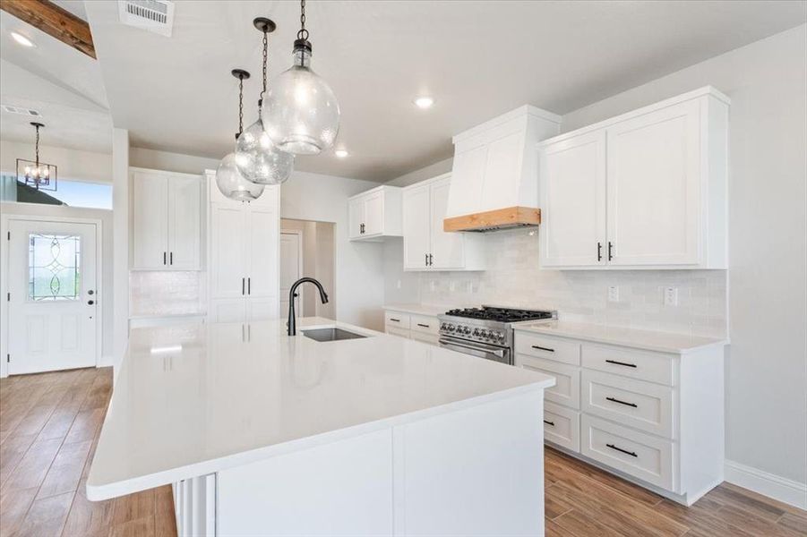 Kitchen with visible vents, an inviting chandelier, a sink, stainless steel stove, and premium range hood