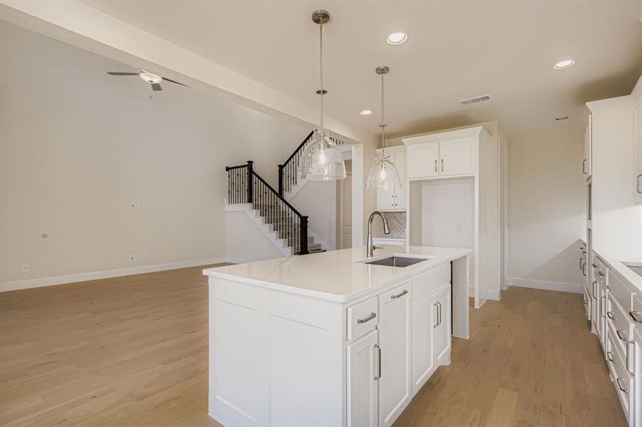 Kitchen with decorative light fixtures, recessed lighting, a center island with sink, light wood-type flooring, and white cabinets Kitchen with decorative light fixtures, recessed lighting, a center island with sink, light wood-type flooring, and white cabinets