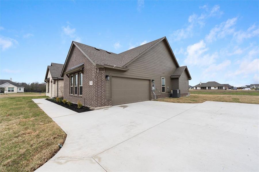 View of side of property featuring a yard, roof with shingles, driveway, brick siding, and an attached garage View of side of property featuring a yard, roof with shingles, driveway, brick siding, and an attached garage