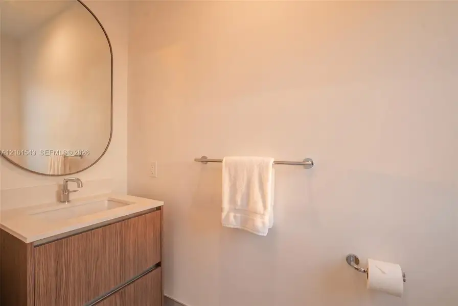 Wood-finish floating vanity with a stone-top integrated basin, polished chrome faucet, and oval wall-mounted mirror, complemented by matching chrome bathroom hardware