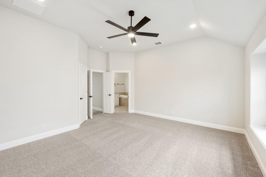 Empty master bedroom with carpet, ceiling fan, vaulted ceiling, and open ensuite bathroom door Empty master bedroom with carpet, ceiling fan, vaulted ceiling, and open ensuite bathroom door
