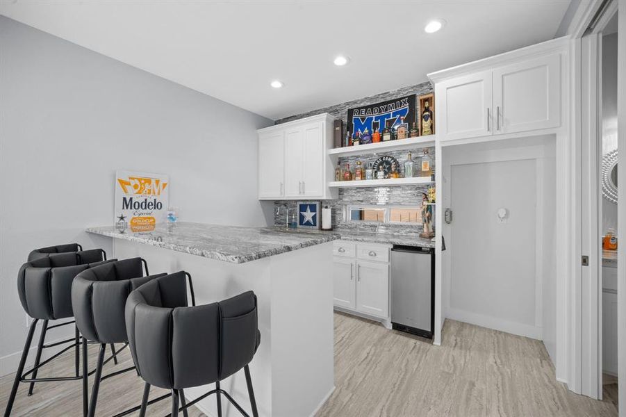 Indoor wet bar featuring open shelves, light stone counters, tasteful backsplash, white cabinetry, and recessed lighting