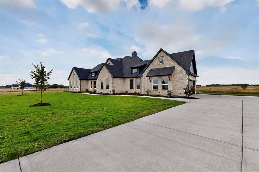 French country inspired facade featuring a front lawn, brick siding, driveway, and a shingled roof French country inspired facade featuring a front lawn, brick siding, driveway, and a shingled roof