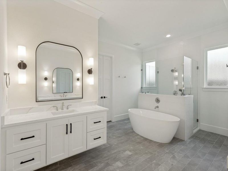 Bathroom featuring a freestanding soaking tub, glass-enclosed shower with multiple showerheads, a vanity with a quartz countertop, and rectangular floor tile Bathroom featuring a freestanding soaking tub, glass-enclosed shower with multiple showerheads, a vanity with a quartz countertop, and rectangular floor tile
