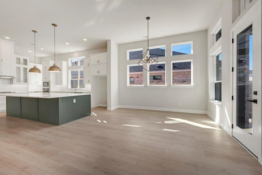 Two tone kitchen with dual tone cabinetry, glass insert cabinets, a large island, light wood-style floors, and a chandelier