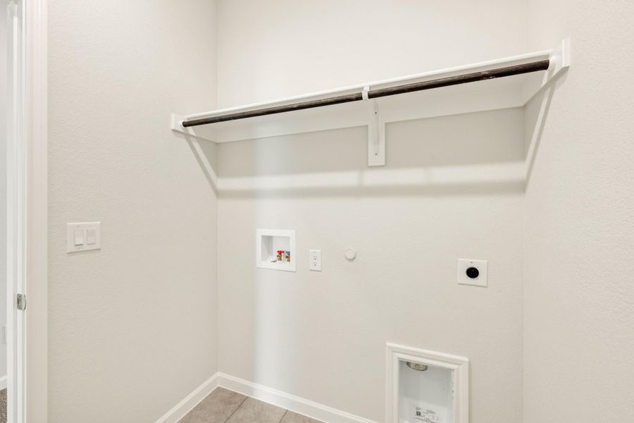Laundry room with wall-mounted shelf, hanging rod, washer hookups, and dryer vent connection on white walls Laundry room with wall-mounted shelf, hanging rod, washer hookups, and dryer vent connection on white walls