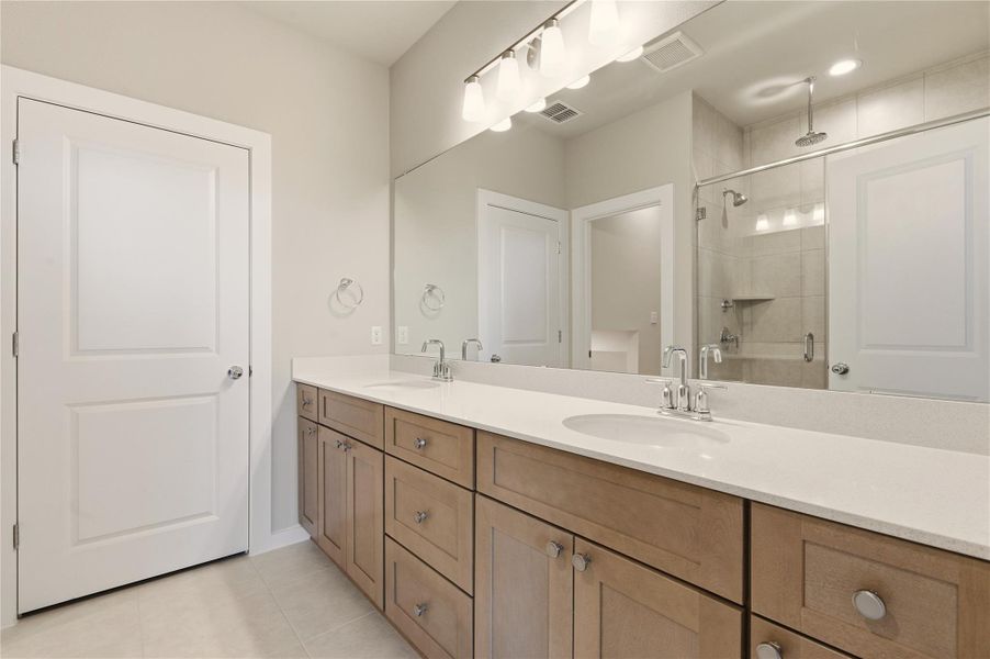 Bathroom with double vanity, a shower stall, and light tile patterned floors