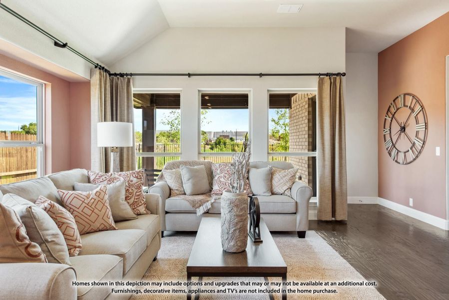 Living room with vaulted ceiling, large windows, hardwood floors, and neutral sofas with pink accent pillows Living room with vaulted ceiling, large windows, hardwood floors, and neutral sofas with pink accent pillows