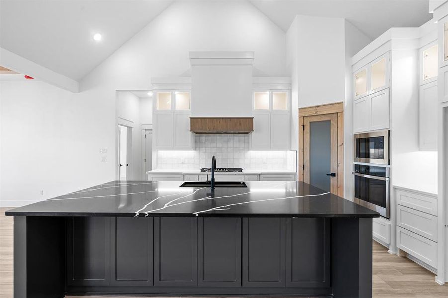 Kitchen with oven, white cabinetry, black microwave, tasteful backsplash, and a spacious island