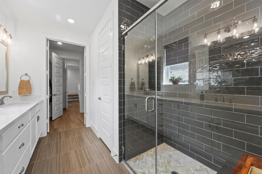 The primary bath showcases a spacious walk-in shower with a semi-framed glass enclosure. The stunning tile work and modern fixtures highlight the home's high-quality finishes.