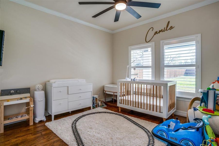 Bedroom with ceiling fan, crown molding, dark wood-type flooring, and a crib