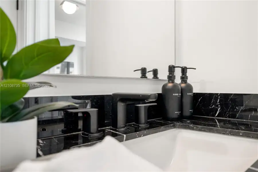 Vanity featuring a dark stone countertop, undermount sink, matte black widespread faucet, and a large wall-mounted mirror Vanity featuring a dark stone countertop, undermount sink, matte black widespread faucet, and a large wall-mounted mirror