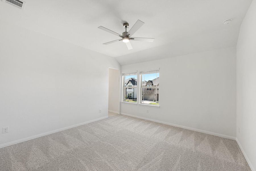Empty bedroom with vaulted ceiling, ceiling fan, carpet flooring, and a window overlooking neighboring homes Empty bedroom with vaulted ceiling, ceiling fan, carpet flooring, and a window overlooking neighboring homes