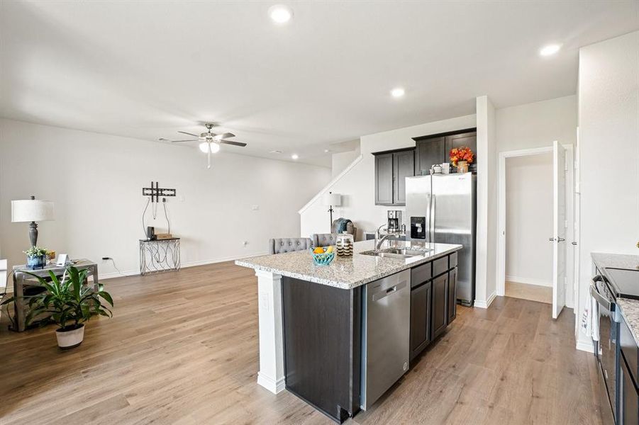 Kitchen with light stone counters, recessed lighting, light wood-style floors, appliances with stainless steel finishes, and a kitchen island with sink Kitchen with light stone counters, recessed lighting, light wood-style floors, appliances with stainless steel finishes, and a kitchen island with sink