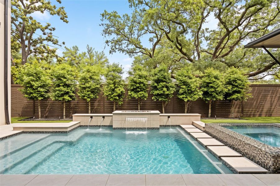 Custom pool and spa with cascading water features, stepping pads, and a fully landscaped privacy backdrop