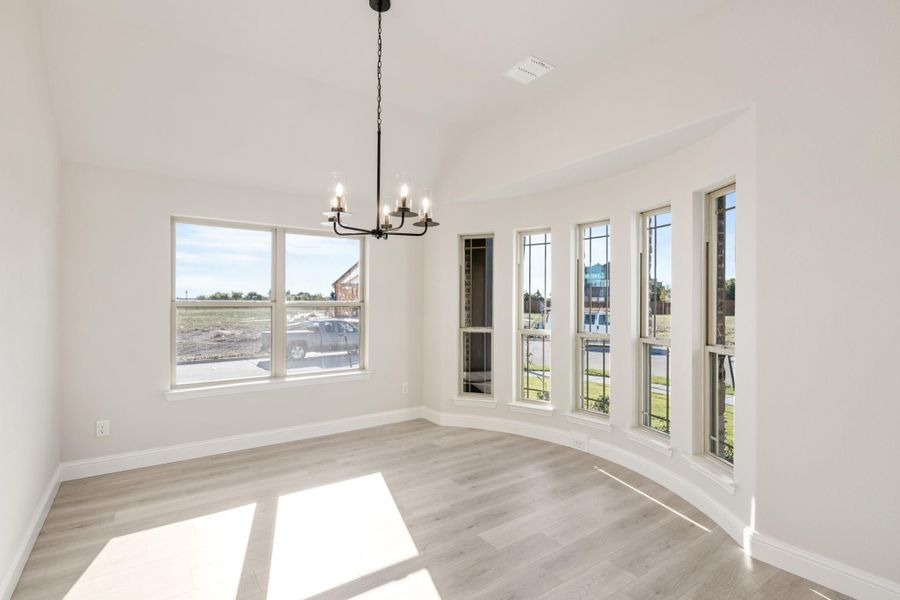 Bright empty dining area with bay windows, chandelier, and light hardwood floors