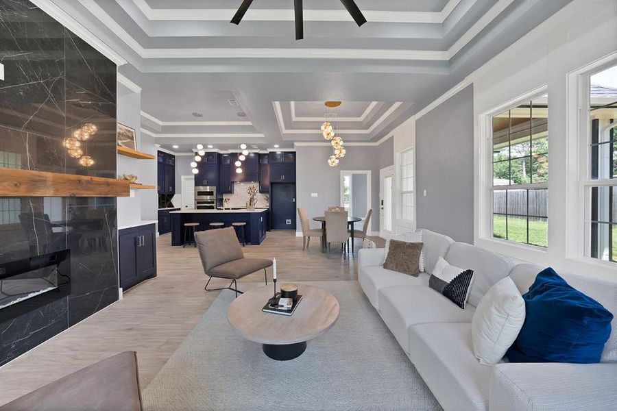 Open-concept living space featuring a black marble-finish fireplace with a wood mantle, wood-finish flooring, and tray ceilings